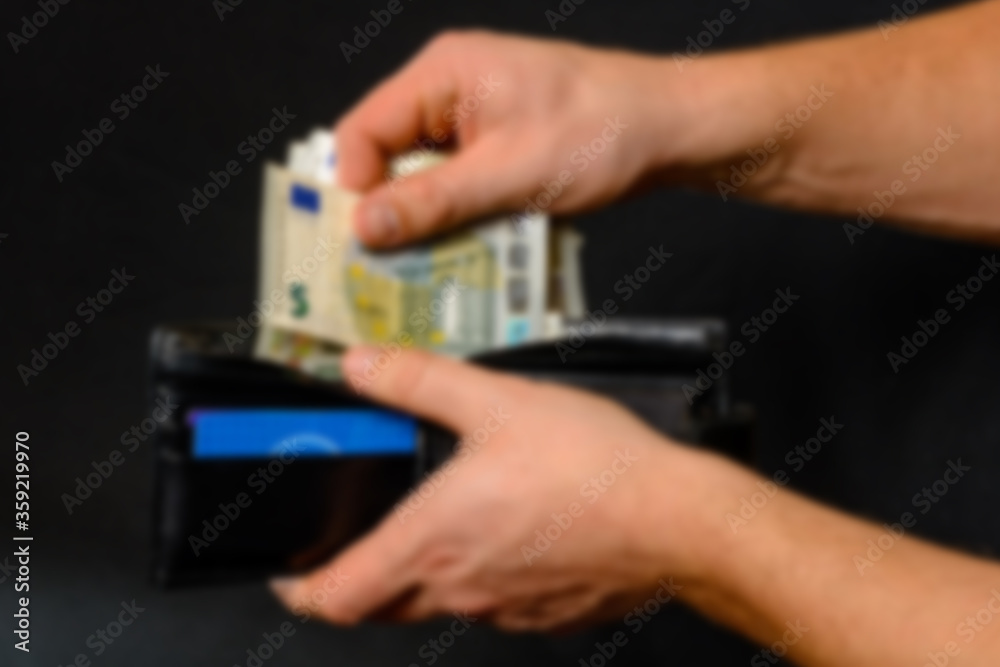 Man hand pulling money from wallet, black background and black wallet. Blurred and defocused image. Man hand pulling money from wallet, black background and black wallet. Blurred and defocused image.
