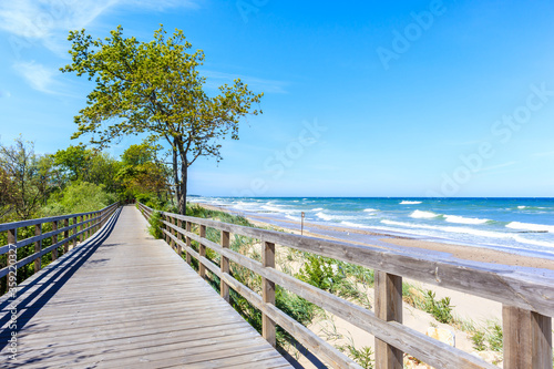 Drewniany chodnik wzdłuż pięknej piaszczystej plaży z błękitnym morzem w pobliżu Kołobrzegu, wybrzeże Morza Bałtyckiego, Polska