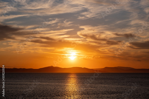 Sunrise, sunset clouds. Twilight, dusk cloudy sky over sea water, mountain silhouette