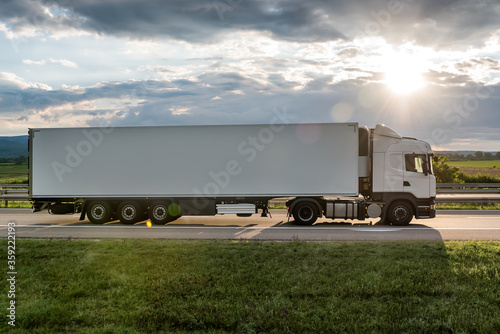 White truck is on highway - business, commercial, cargo transportation concept, beautiful sunset sky, clear and blank space - side view