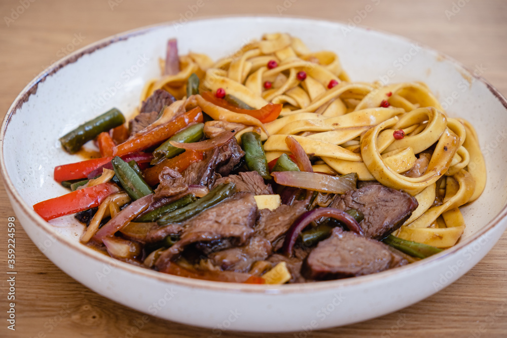 Italian spaghetti pasta with beef and bean pods, carrots in a deep plate on a wooden table in a restaurant. Italian spaghetti pasta with beef and bean pods, carrots in a deep plate on a wooden table in a restaurant.