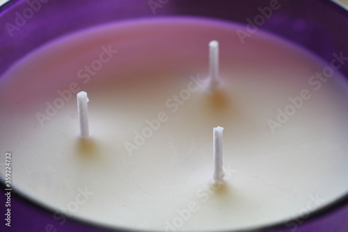 A close up image of three wick candle in a bright purple glass jar. 