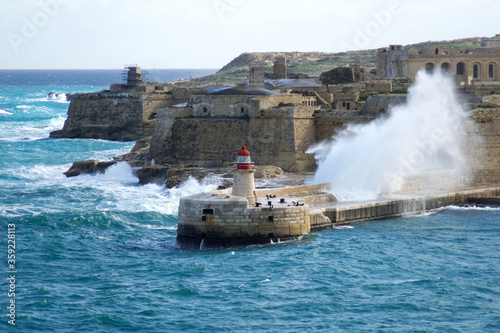 VALLETTA, MALTA - DEC 31st, 2019: View from Fort St Elmo on to the Ricasoli Grand Harbour East Breakwater and red lighthouse during strong waves
