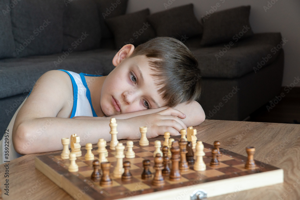 The serious child lost in thought playing chess. Playing board games, on coronavirus quarantine. The child playing chess.