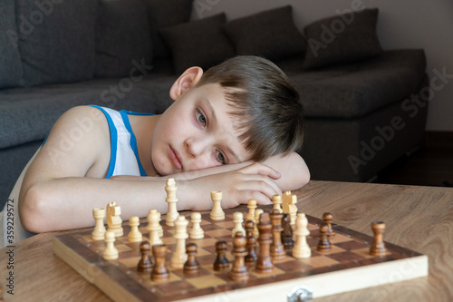 Obraz na płótnie The serious child lost in thought playing chess. Playing board games, on coronavirus quarantine. The child playing chess. w salonie