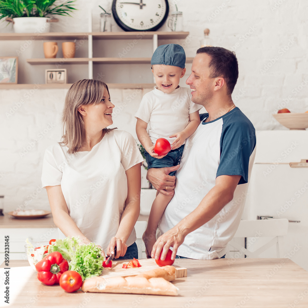 Happy family of mom, son and father are cutting vegetables on salad and having fun together in