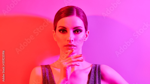High Fashion. Model in colorful neon light, make-up. Sexy girl, stylish hair, trendy makeup. Party neon pink purple style. Glamour beauty Woman face, fashionable portrait, bright make up