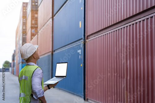 inspection engineer wear helmet and uses laptop computer to check the accuracy of the container before exporting or receiving the product.Prepare for importing or exporting products in container yard.