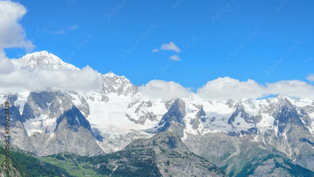 View of the highest mountain peak in Italian Alps, Monte Bianco (meaning White Mountain), in Courmayeur valley, with white moving clouds and blue sky on the background View of the highest mountain peak in Italian Alps, Monte Bianco (meaning White Mountain), in Courmayeur valley, with white moving clouds and blue sky on the background