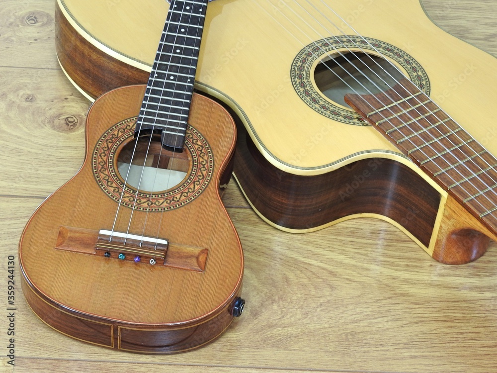Close-up of an acoustic guitar and a Brazilian string musical instrument: cavaquinho, on a wooden surface. They are widely used to accompany samba and choro, two popular Brazilian rhythms. Top view. Close-up of an acoustic guitar and a Brazilian string musical instrument: cavaquinho, on a wooden surface. They are widely used to accompany samba and choro, two popular Brazilian rhythms. Top view.
