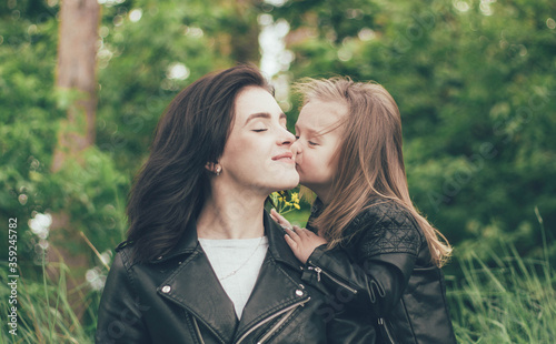  girl kisses mom on the cheek in nature, daughter and mom in identical leathers