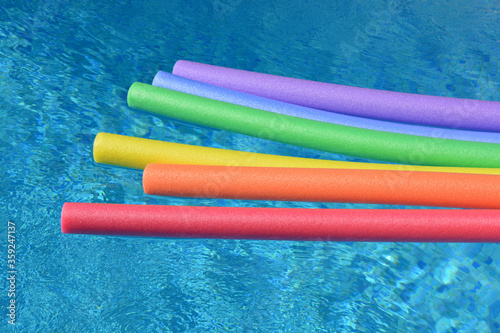 Rainbow coloured pool noodles floating in a swimming pool on a bright and sunny day.