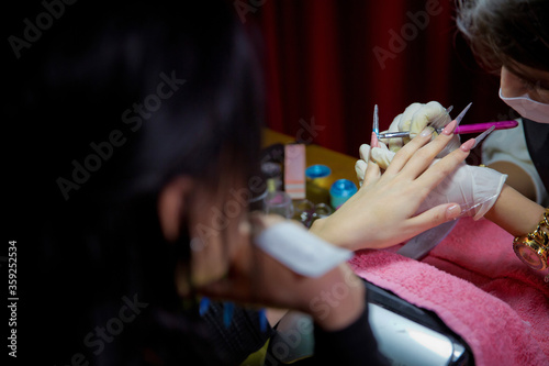Woman in a nail salon receiving a manicure by a beautician . Manicure process in beautiful salon . Closeup of Woman applying nail varnish to finger nails . Manicure hands salon .