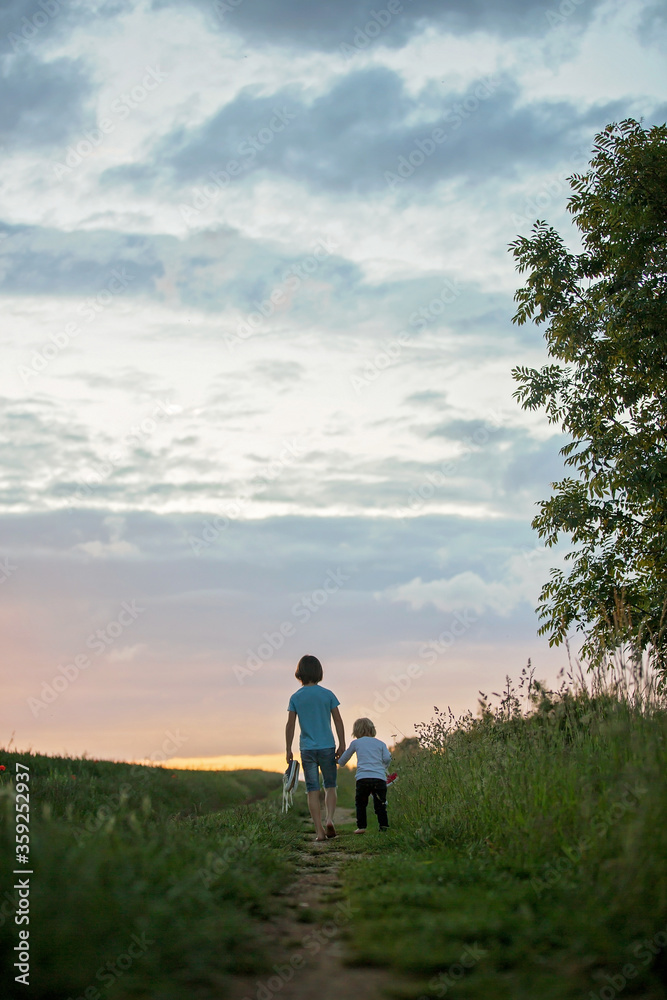 Happy child, holding pair of sneakers in hands, walking on a rural path