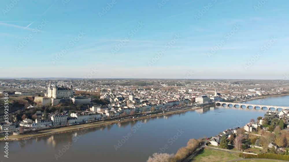 Saumur town skyline with medieval castle and church reflecting on the river at sunrise, Loire Valley, France. Aerial drone dolly shot, pedestal  rising up, revealing landscape