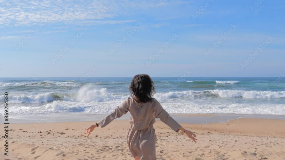 Woman in dress with arms raised up at the beach enjoying sea view
