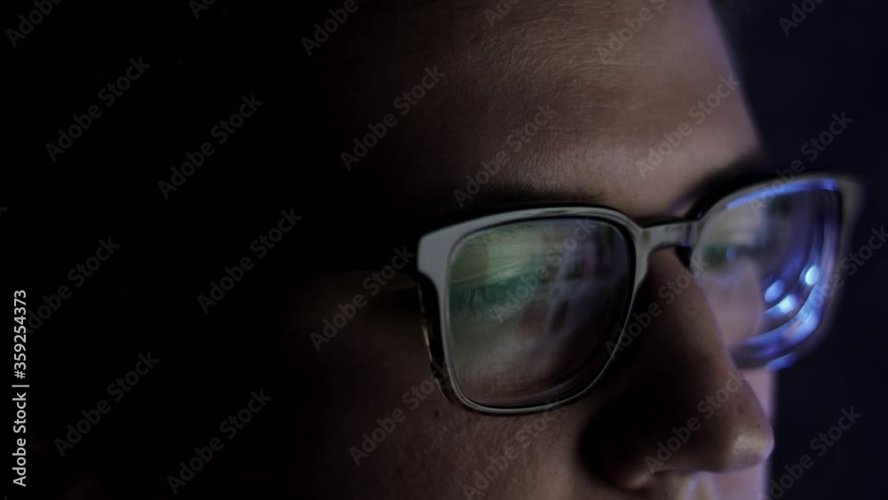 Man in eyeglasses late at night scrolling in front of laptop. Coder, programmer or developer using laptop in dark. Close up of glasses with reflection of computer screen. Man in eyeglasses late at night scrolling in front of laptop. Coder, programmer or developer using laptop in dark. Close up of glasses with reflection of computer screen.