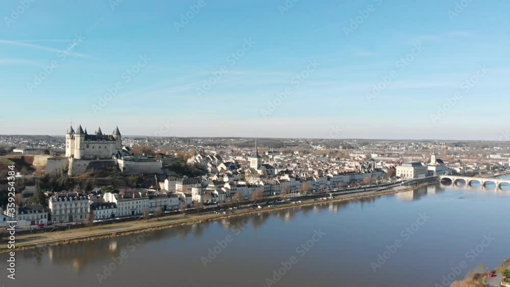 Saumur town skyline with medieval castle and church reflecting on the river at sunrise, Loire Valley, France. Aerial drone dolly shot and panning, revealing town and river bridge Saumur town skyline with medieval castle and church reflecting on the river at sunrise, Loire Valley, France. Aerial drone dolly shot and panning, revealing town and river bridge