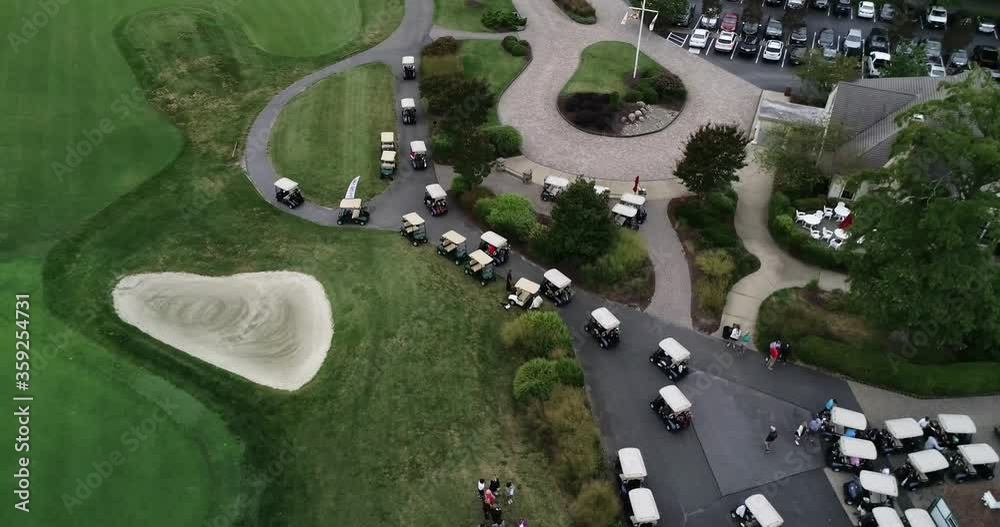 Drone video following a long row of golf carts driving along a concrete path before a golf tournament in Maryland