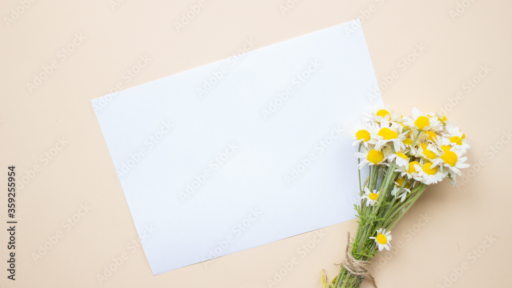 Wedding desktop mock up with blank white paper card and chamomiles flowers bouquet branch on beige background.Empty copy space.Styled stock photo,web banner.Flat lay,top view.Spring or summer concept