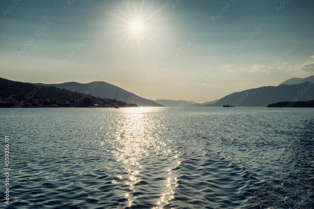 The bright sun on the sea with a view of the mountains. Adriatic Sea in Montenegro. Tourism and travel. Space for text.