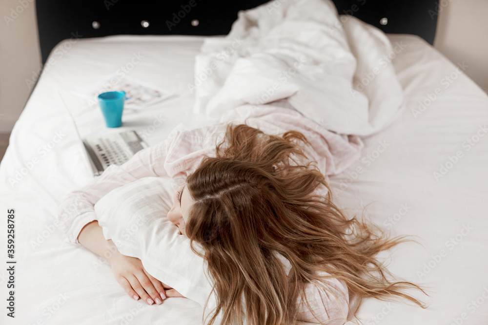 A young attractive girl in pajamas is lying on the bed at home, next to a laptop and a Cup of coffee. The girl works before going to bed