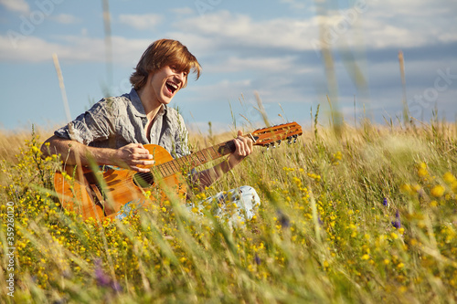 handsome young man with acoustic guitar summer outdoors.