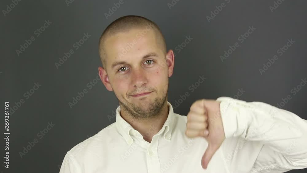 Funny handsome guy shows thumb down expressing his disapproval. Portrait on a gray background. Funny handsome guy shows thumb down expressing his disapproval. Portrait on a gray background.