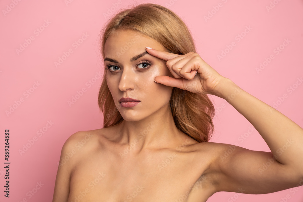 Pretty, nude, natural girl thinking about tightening, plastic operation, holding fingers near eyes, looking at camera isolated on pink background, wellbeing, wellness concept Pretty, nude, natural girl thinking about tightening, plastic operation, holding fingers near eyes, looking at camera isolated on pink background, wellbeing, wellness concept