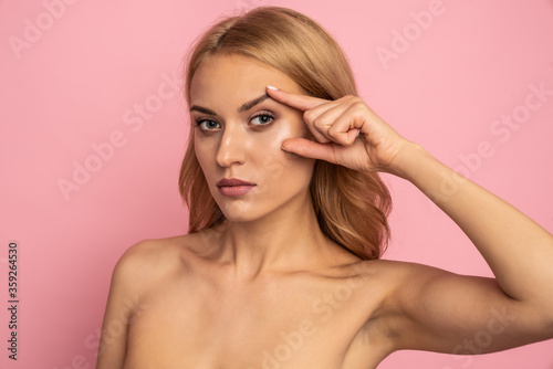 Pretty, nude, natural girl thinking about tightening, plastic operation, holding fingers near eyes, looking at camera isolated on pink background, wellbeing, wellness concept