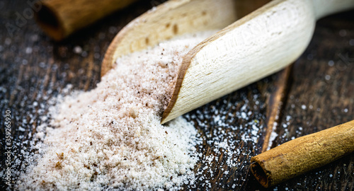 wooden measuring spoon with powdered cinnamon and refined sugar, used as ingredients for sweets and desserts.