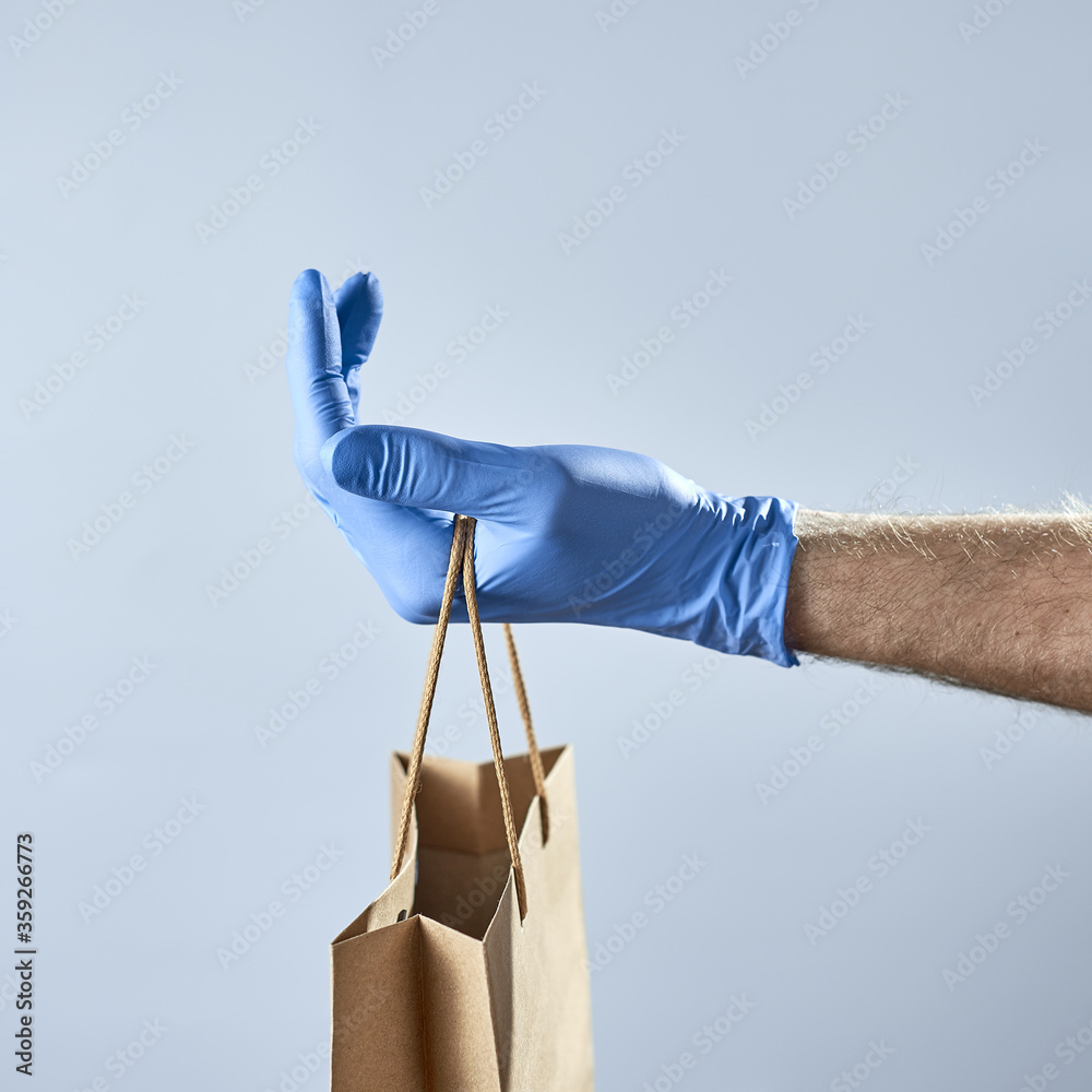 Hand in blue rubber gloves holds a paper bag. Concept of safe delivery during a pandemic.
