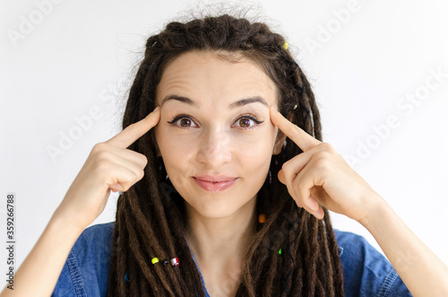 funny girl with dreadlocks holds fingers at the temples and shows a gesture think