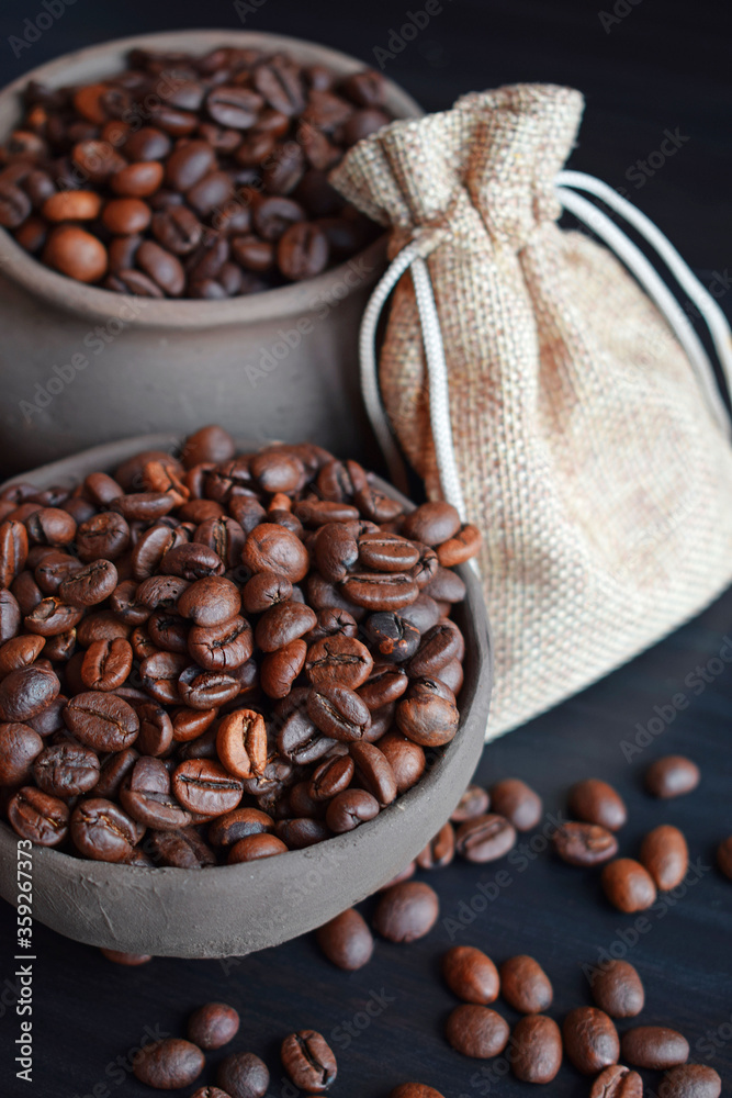 Fototapeta premium Coffee beans in an earthenware dish and a bag on a wooden table.