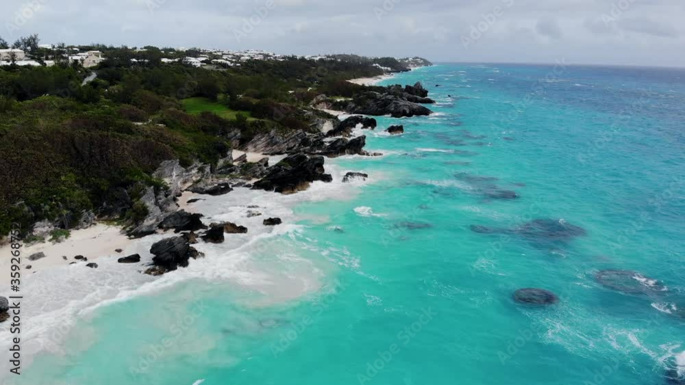 Flying over the beautiful white sand beach of Bermuda with breathtaking clear turquoise Caribbean ocean waves.