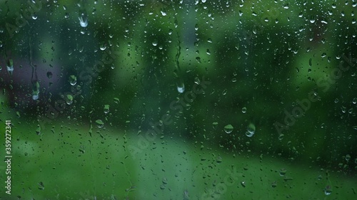 raindrops patter against a window slide, in the background you see a blurred garden