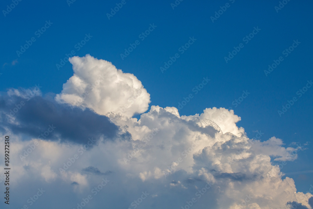 White contrasting clouds backlit by the sun on a blue summer sky. Background. White contrasting clouds backlit by the sun on a blue summer sky. Background.