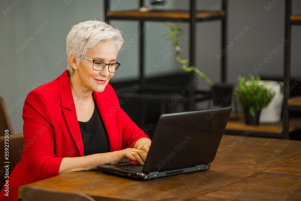 beautiful stylish aged woman in a red jacket works in the office with a laptop beautiful stylish aged woman in a red jacket works in the office with a laptop