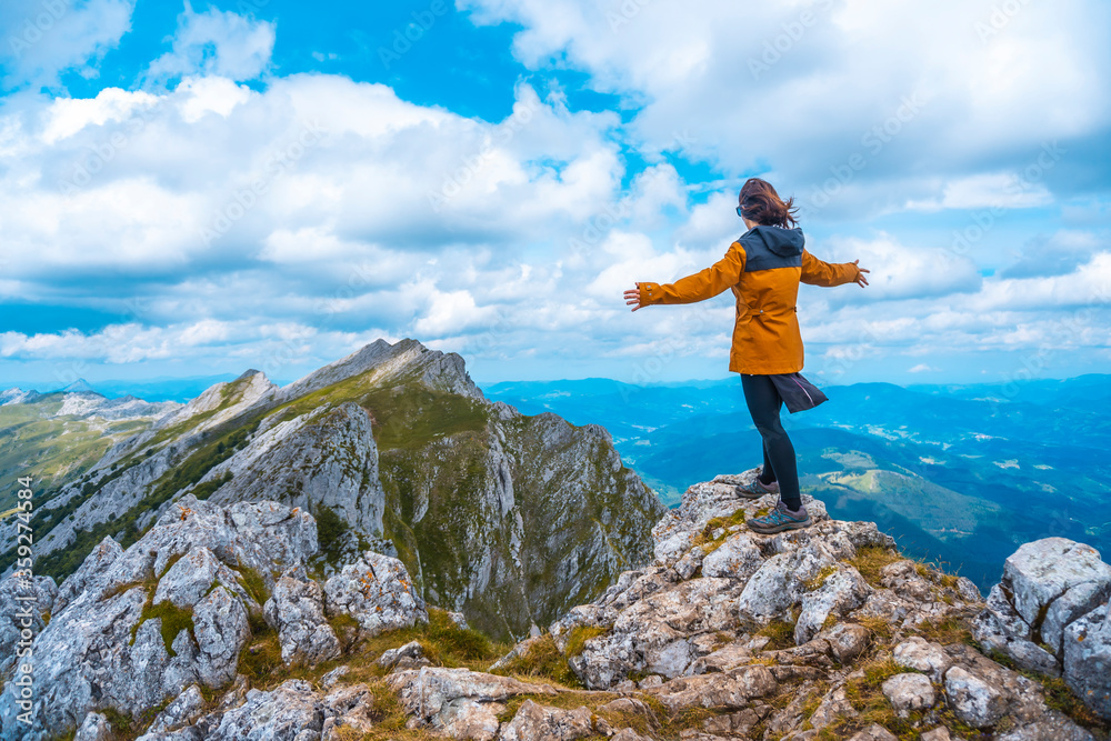 Obraz premium Mount Aizkorri 1523 meters, the highest in Guipúzcoa. Basque Country. Ascent through San Adrián and return through the Oltza fields. A young woman in yellow with open arms