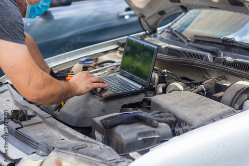 auto mechanic with protective mask diagnosing car with black laptop © Gegham