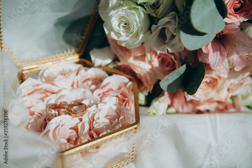 golden shiny wedding rings lie in a decorative box next to a wedding bouquet