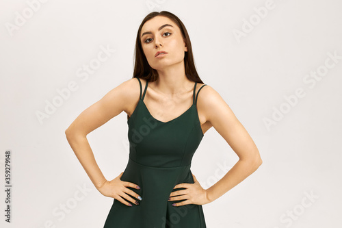 Isolated image of gorgeous fashionable young woman with fair skin and long straight hair getting dressed before going out  wearing strap summer dress  holding hands on her waist  having confident look