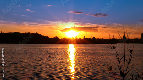 Amazing sunrise over a lake. Rays of the sun reflecting on the water. Silhouette of vegetation in the foreground.