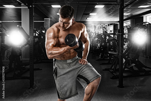 Brutal strong muscular bodybuilder athletic man pumping up muscles with dumbbell in the gym. Workout bodybuilding concept. 