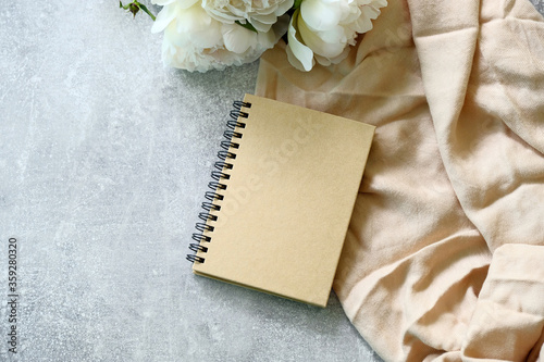 Kraft paper notebook or wedding photo album with peonies on concrete stone table. Flat lay, top view.