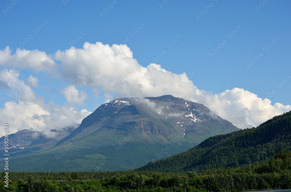 tall majestic mountain surrounded by small floating clouds in summer