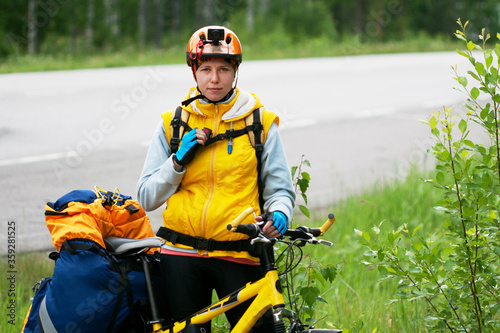 Young woman in sportive clothes and helmet travelling alone by bike wiith action camera, pannier bag and drinking system. Solo travell, road trip, responsible travelling and hyper-local travel concept