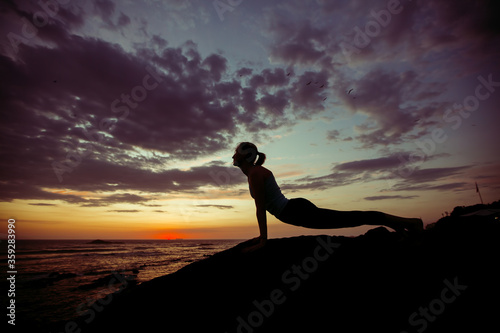 Fototapeta Naklejka Na Ścianę i Meble -  Young fitness woman exercise on the ocean coast at twilight. Yoga and training. .