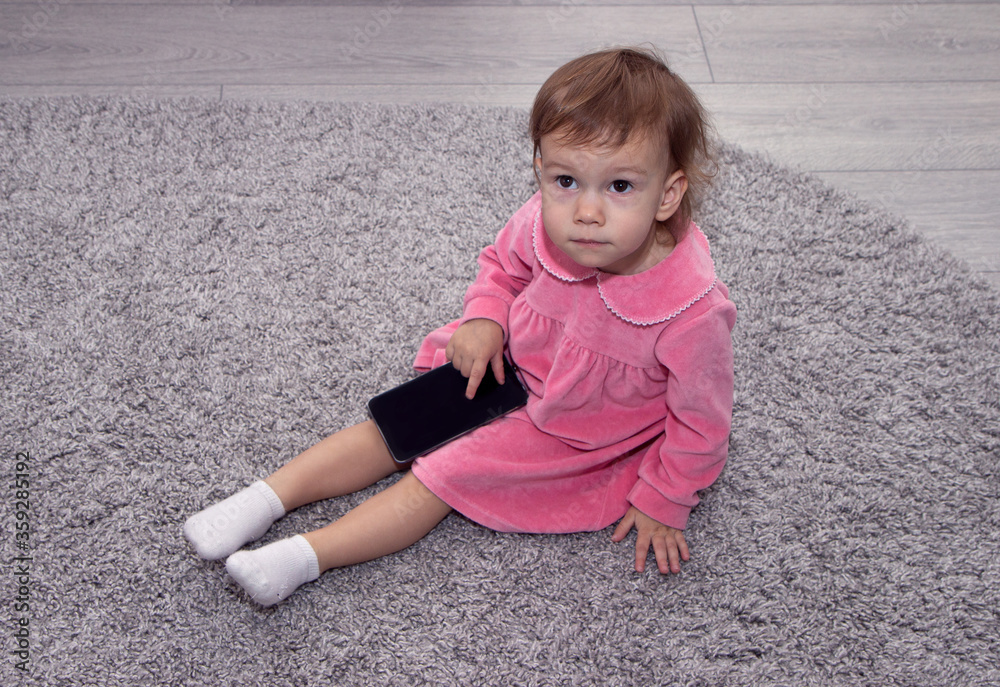 Fototapeta premium beautiful little girl with a smartphone on the carpet in her room.