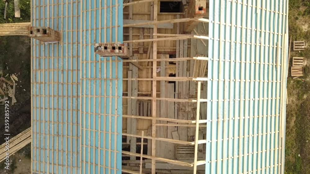 Aerial view of a brick house with wooden roof frame under construction and foundation for a new project.